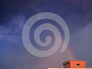 Rainbow over the house rises to dark heavy rain clouds