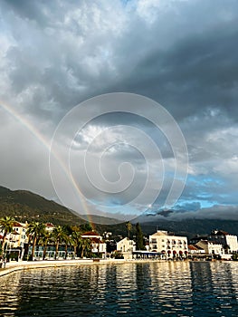 Rainbow over the houses on the sea coast at the foot of the mountains against a cloudy sky