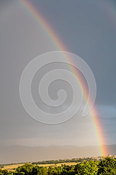 Rainbow over a quaint village and meadows, after the rain, copy space, wallpaper.