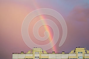 Rainbow over the roof of a multi-storey city house in the evening pink sunset sky after the rain, summer fantastically beautiful