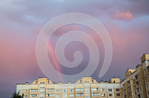 Rainbow over the roof of a multi-storey city house in the evening pink sunset sky after the rain, summer fantastically beautiful