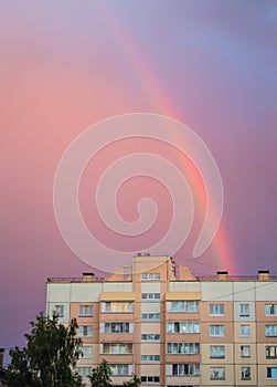 Rainbow over the roof of a multi-storey city house in the evening pink sunset sky after rain, summer fantastically beautiful