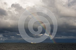 Rainbow over Sea, dark clouds and lighted container ship on Baltic Sea