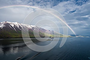 The rainbow over the sea near the snowy mountains and an isolated ship