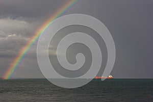 Rainbow over the sea. The sun`s rays illuminate the ship.