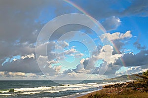 Rainbow over the sea and tropical beach with umbrellas chairs and tables.