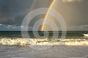 Rainbow over the sea and tropical beach with umbrellas chairs and tables.