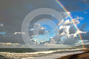 Rainbow over the sea and tropical beach with umbrellas chairs and tables.