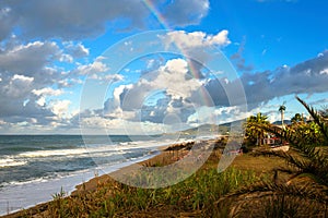 Rainbow over the sea and tropical beach with umbrellas chairs and tables.