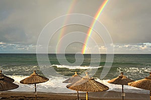 Rainbow over the sea and tropical beach with umbrellas chairs and tables.