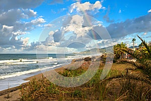 Rainbow over the sea and tropical beach with umbrellas chairs and tables.