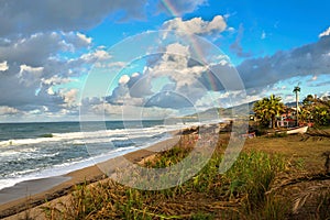 Rainbow over the sea and tropical beach with umbrellas chairs and tables.