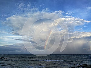 Rainbow over the sea with waves splashes and blue sky