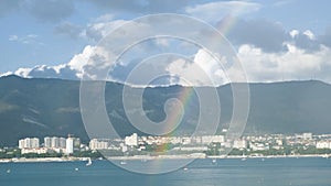 Rainbow over sea with yachts and mountain coast. Concept. Seascape with rainbow on background of coast with town