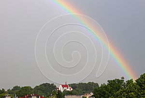 Rainbow over the temple in a dark and rainy sky. Unfavorable weather conditions. A beautiful atmospheric phenomenon of refraction
