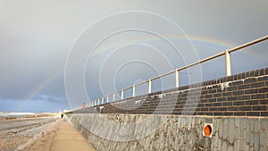 Rainbow over a UK beach and sea ocean defence brick wall