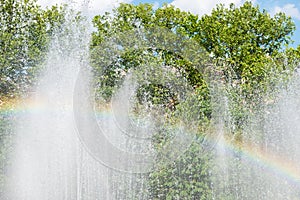 Rainbow over water in fountain with green trees on background