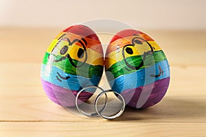 Rainbow painted eggs with engagement rings on wooden table. LGBT concept