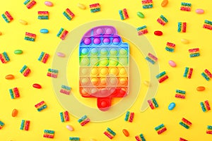 Rainbow Pop it fidget toy next to the colorful marmalade candies on yellow background. photo