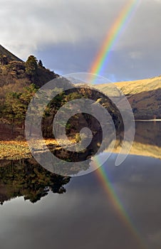 Rainbow reflected in a still waters of lake Llyn Gwynant with forest and mountains