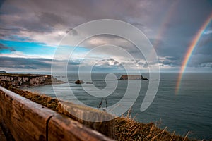Rainbow shining between rainy clouds, sea and cliffs near Ballintoy in Northern Ireland, with Sheep Island in the background