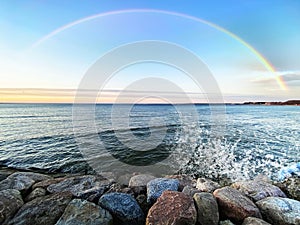 Rainbow at sky Sunset at sea water green wave splash and seafront stones with pink blue colorful sunset panorama