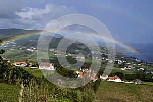 A rainbow sprawling across a green field into the sea on the faial island