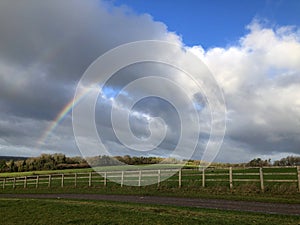 Rainbow, storm clouds and blue sky over rural landscape