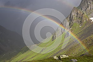 Rainbow stretching over a mountain valley in front of dark thunder storm-