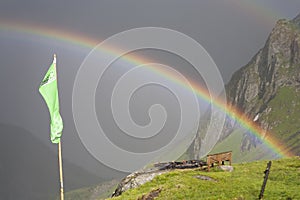 Rainbow stretching over a mountain valley in front of dark thunder storm.