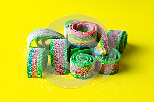 Rainbow stripes of sweets made of sour jelly in sugar sprinkles on a yellow background. Top view.
