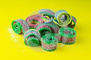 Rainbow stripes of sweets made of sour jelly in sugar sprinkles on a yellow background. Top view.