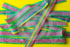 Rainbow stripes of sweets made of sour jelly in sugar sprinkles on a yellow background. Top view.