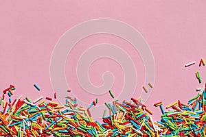 Rainbow sugar sprinkle dots, decoration for cake and bakery on colored backdrop. Colorful sprinkles on pink background.