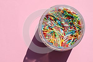 Rainbow sugar sprinkle dots, decoration for cake and bakery in jar on colored backdrop. Colorful sprinkles on pink background. Con