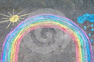 Rainbow sun and clouds with rain drops painted with colorful chalks on ground or asphalt in summer. Creative leisure for