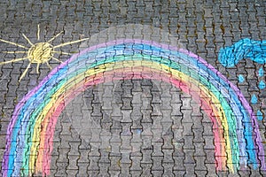 Rainbow sun and clouds with rain drops painted with colorful chalks on ground or asphalt in summer. Creative leisure for