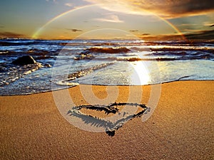 Rainbow at sunset sea and heart symbol on sand romantic nature landscape