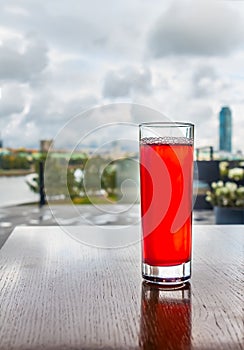 A rainbow transparent glass with red cranberry juice and the beautiful reflections is on a wooden table