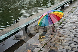 rainbow umbrella on cobblestone street in border water by rainy day