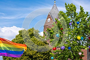 Rainbowflag in front of church and colorful lampions in tree.