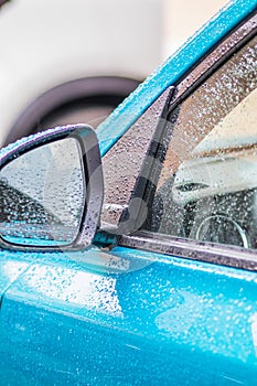 Raindrops on the car. Car element with raindrops close-up. Doors, mirror and glass of a blue car in raindrops. Big raindrops on