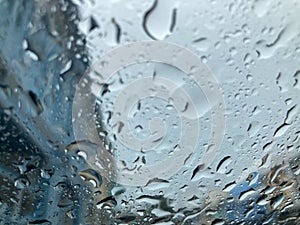 Raindrops on car`s front windshield and blurred blue buildings view