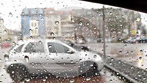 Raindrops on car window with blurry background of city streets background on rainy day in winter