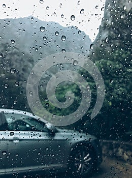 Raindrops on the clean car glass image with silver color car on the background. Deep autumn cold rainy foggy day photo on the