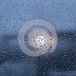 Raindrops on a clear glass surface create a textured pattern with varying sizes. The