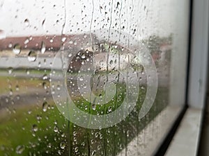 Raindrops cling to a windowpane, creating intricate patterns and distorting the muted view beyond.