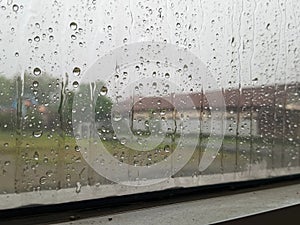 Raindrops cling to a windowpane, creating intricate patterns and distorting the muted view beyond.