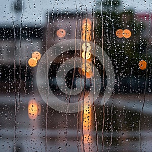 Raindrops create patterns on a window, blurring the view of city lights in the