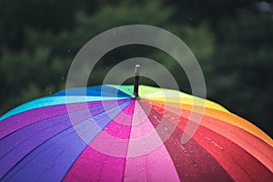 Raindrops fall from the sky onto a rainbow-colored umbrella. Light rain.